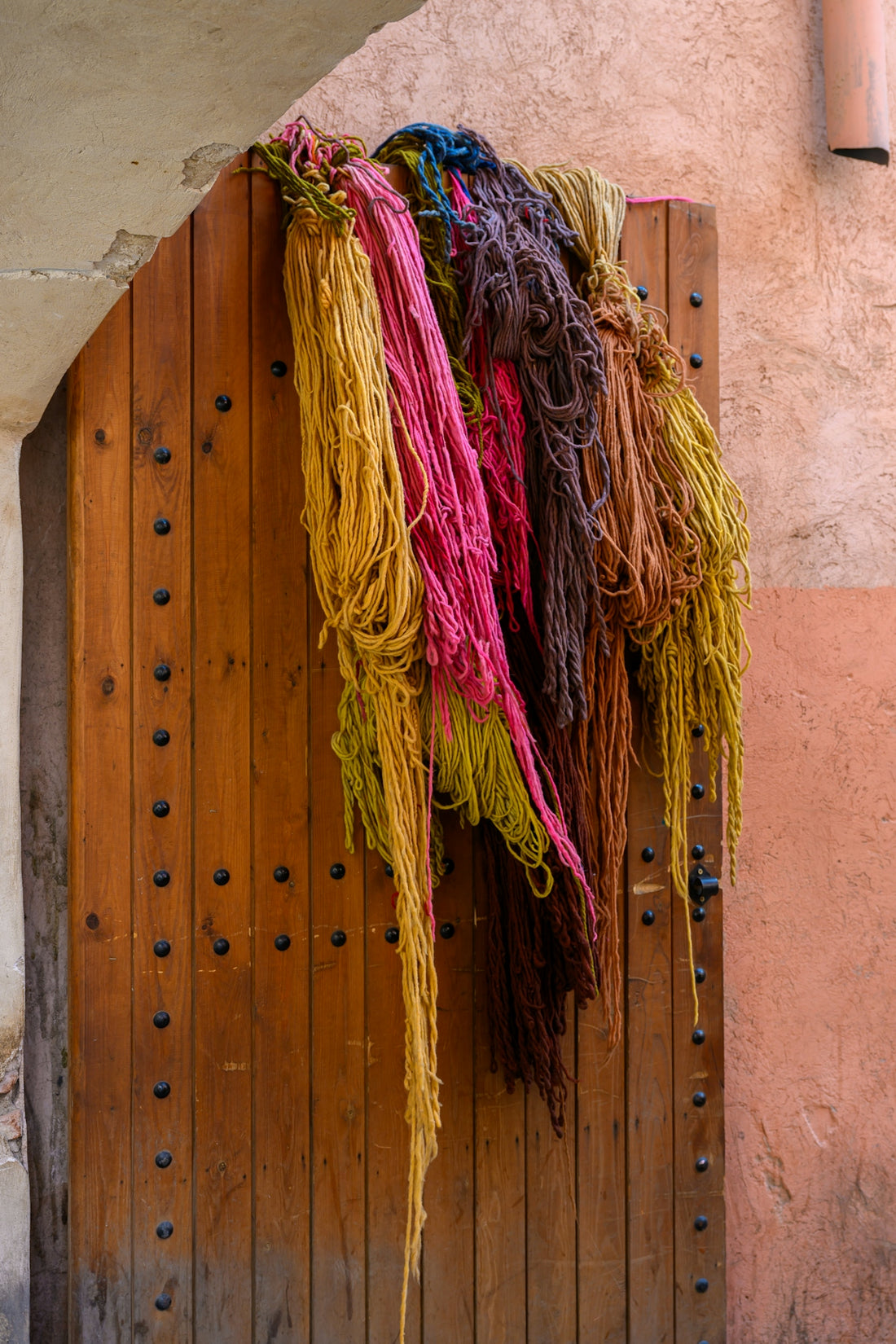 Colored yarn hangs from a rustic wooden door.