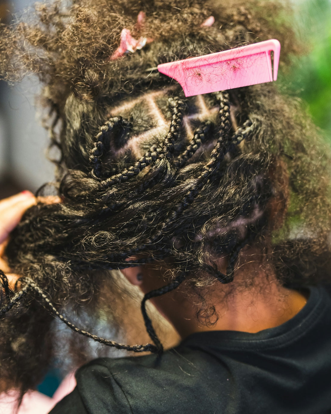 Stylist braiding dark, curly hair with a pink comb.