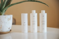 three bottles of lotion sitting on a table next to a potted plant