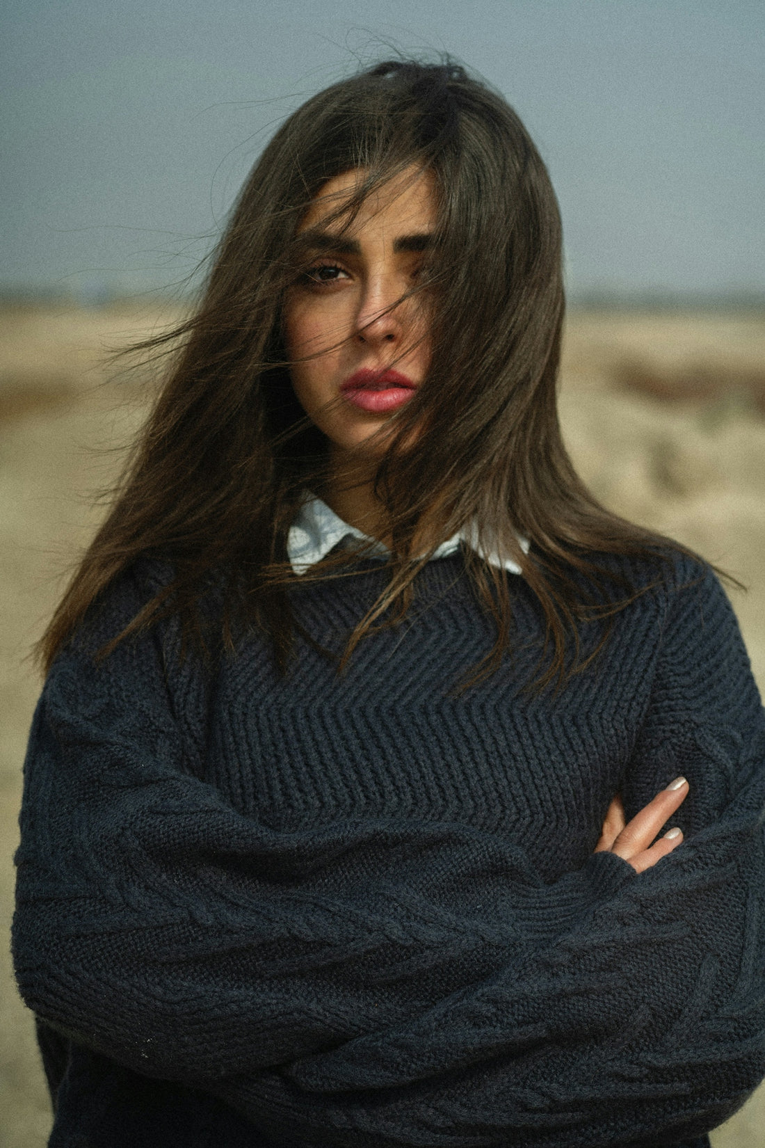 a woman with her arms crossed standing in a field