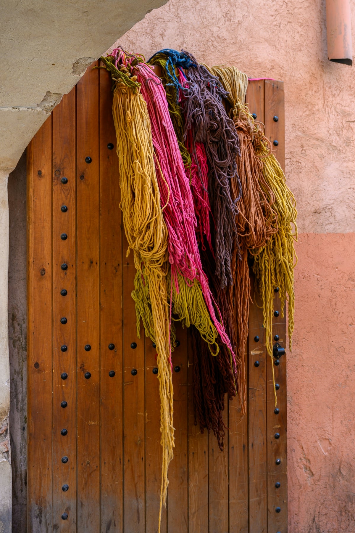 Colored yarn hangs from a rustic wooden door.