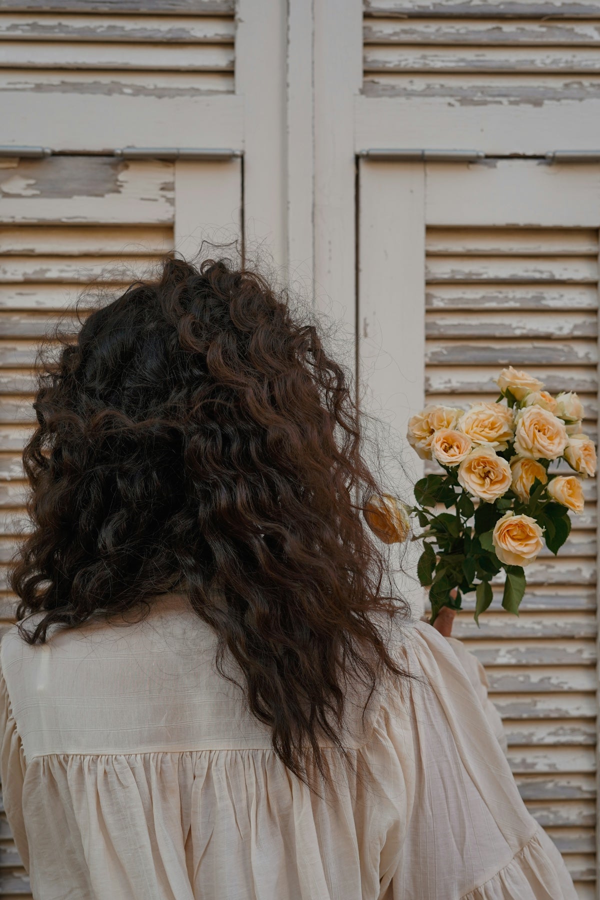Woman holds flowers in front of a shuttered door.